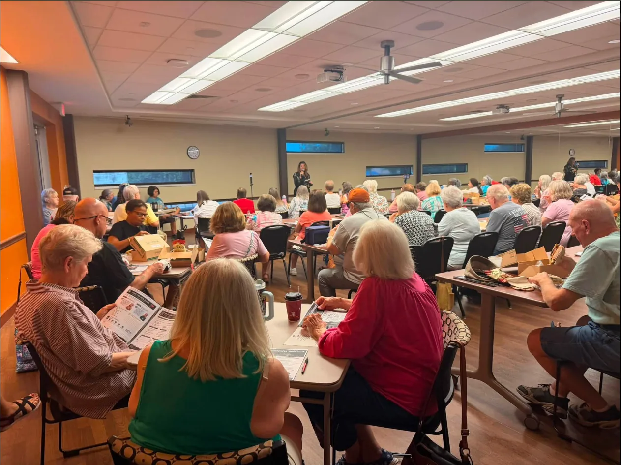Seniors filling a community room at the North Richland Hills Senior Center, working through Silver Streak fraud-awareness workbooks while Sherri Combs presents.